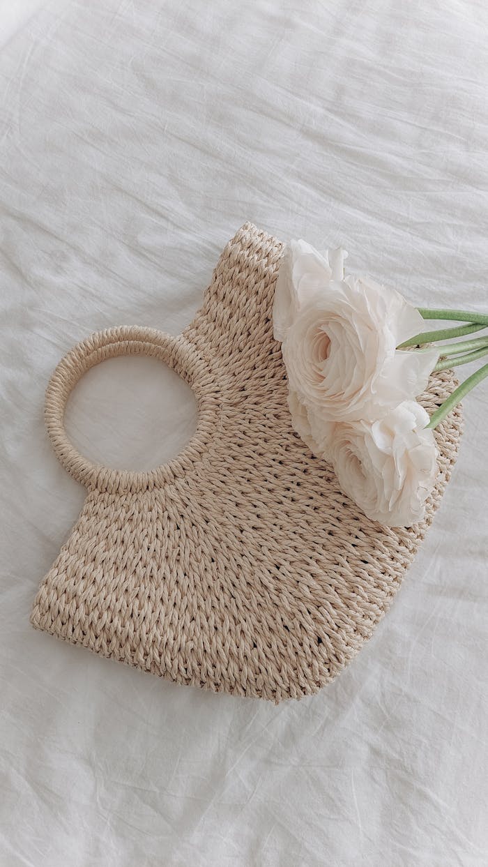 services-01 Minimalist shot of a straw handbag with delicate white flowers on a white sheet, showcasing elegance and simplicity.