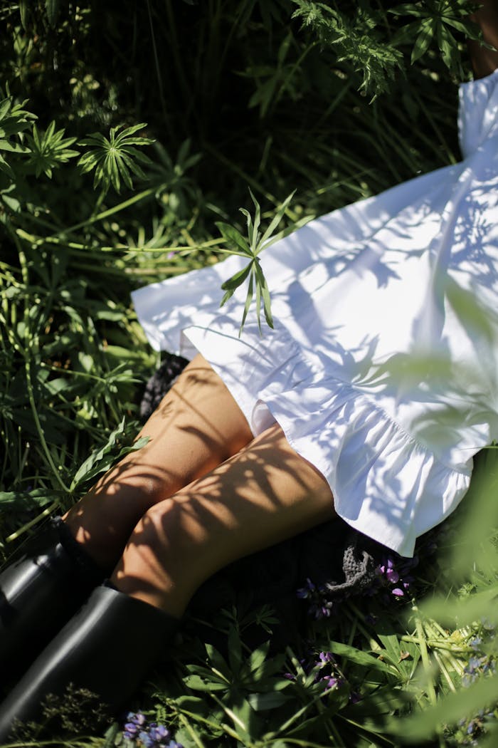 A woman in a white dress enjoying nature surrounded by greenery and shadows.